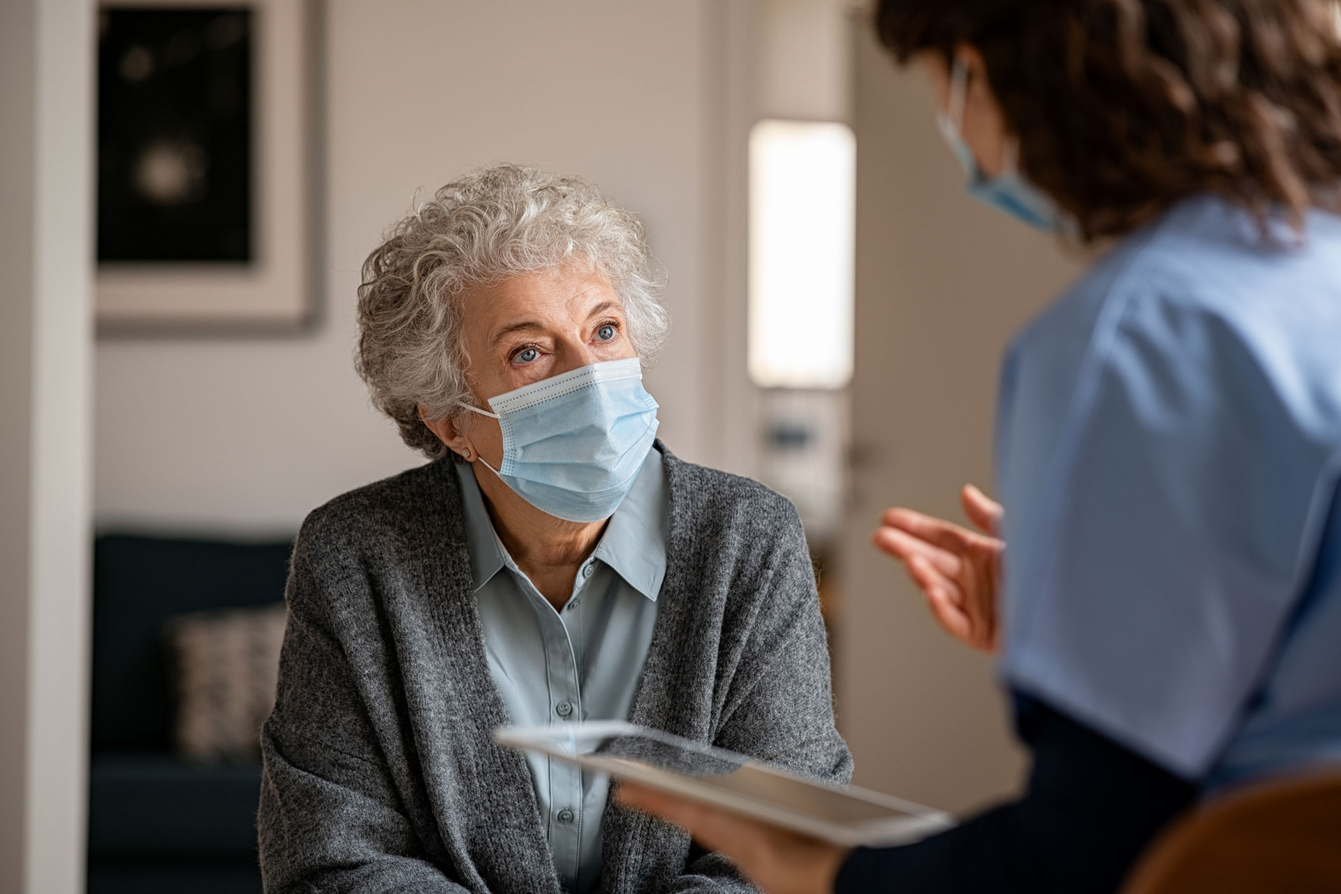 nurse speaking with senior female at nursing home, both wearing masks