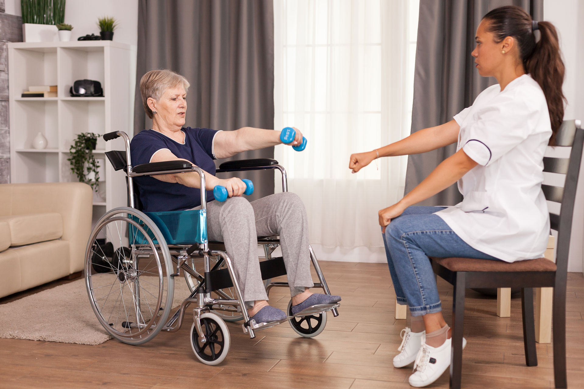 physical therapist helping senior woman in wheelchair lift weights