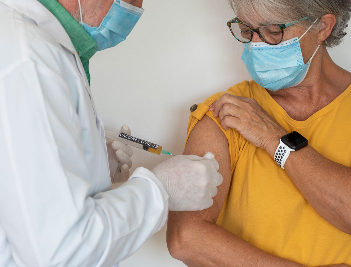 doctor injecting COVID-19 vaccine into senior female