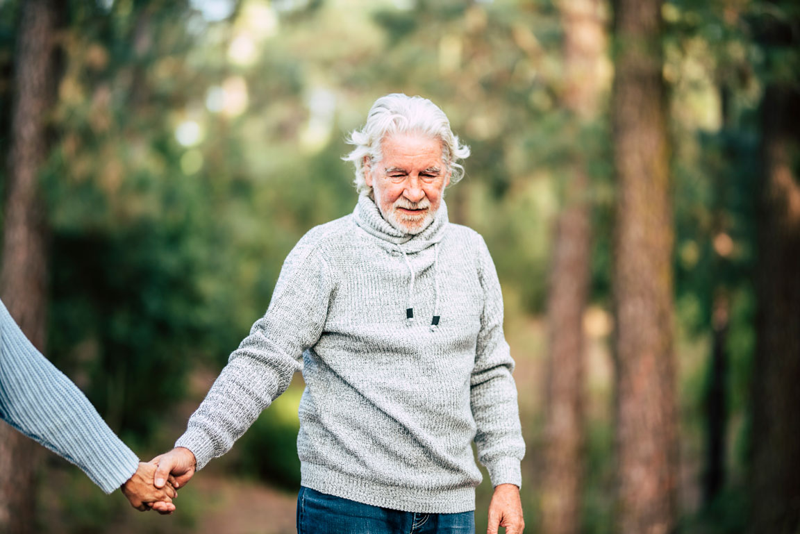 senior male walking in woods holding hands
